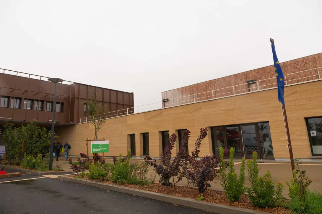 Vue de la façade du collège en acier corten et du gymnase en pierre massive et bois